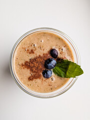 Healthy breakfast smoothie in a glass, topped with fresh blueberries, cinnamon, and a mint leaf,...