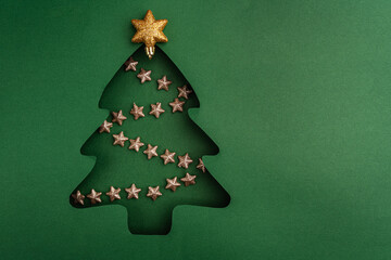 Green paper cutout of a Christmas tree filled with a garland of small glittering gold stars in a festive and minimal holiday design.. Ideal for festive greeting cards, holiday banners