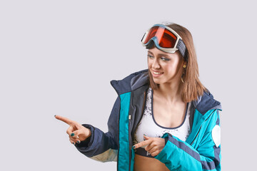 Young caucasian female in ski gear pointing with smile wearing goggles and blue jacket.