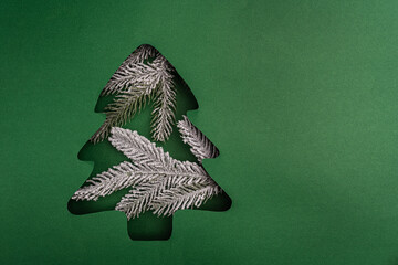 Snow-dusted pine branches fill a green Christmas tree-shaped paper cutout, creating a festive and natural winter holiday composition. Ideal for festive greeting cards, holiday banners