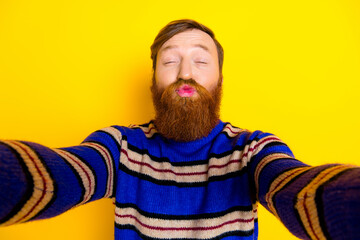 Cheerful young man with red beard happily poses on bright yellow background wearing a striped...