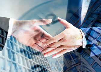 Business partners shaking hands against office buildings, multiple exposure with clock. Deal,...