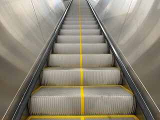 Empty escalator with yellow safety lines rising upward inside a modern building, photographed in...