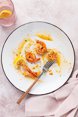the remains of fried shrimp in oil with spices, on a white plate, with a fork, there are no people,