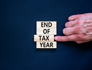 End of tax year symbol. Concept words phrase End of tax year on beautiful wooden blocks. Beautiful black paper background. Businessman's hand. Business End of tax year concept. Copy space.