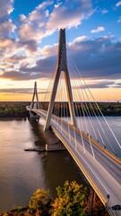Obraz premium A magnificent cable-stayed bridge spans a tranquil river at sunset, showcasing architectural elegance against a vibrant sky.