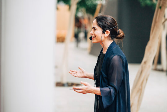 Side view of smiling female speaker wearing headset talking at summit in convention center
