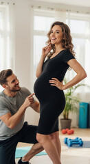 Pregnant woman with partner in black dress at home with exercise equipment. Fitness couple maternity session for prenatal wellness and home workout content
