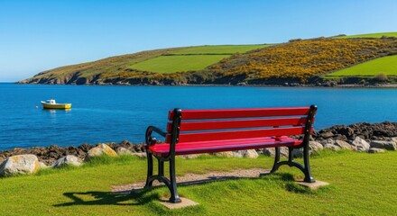 A red bench overlooks the ocean with a yellow boat and green hills on a bright sunny day scene