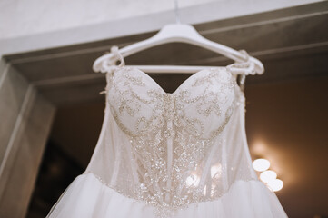 Wedding photo of part, element of white lace dress hanging on hanger in hotel room in morning.