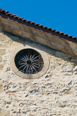Circular stone window with decorative wrought iron grille on old church wall under blue sky