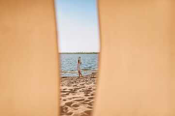 Young barefoot woman in a white sundress walks on the sand against the backdrop of the sea in summer. Photography, portrait.