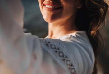 Photograph, portrait of details, elements of the face of a curly beautiful smiling woman on the beach against the backdrop of the sea, ocean in a white sundress, dress at sunset.