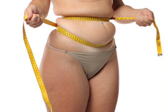 Studio shot of obese woman squeezing waist fat with tape measure for weight loss and body measurement on white background.