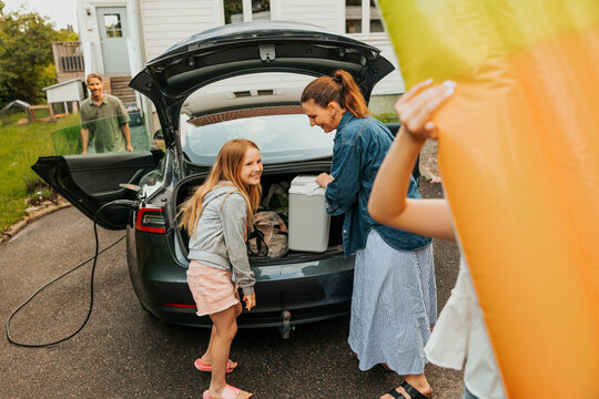 Smiling girl loading car trunk with mother on driveway for summer holiday