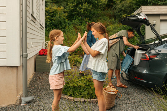 Sister playing clapping game while parents loading car trunk in back yard