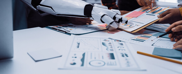 A robot arm assists a human team during a collaborative meeting, analyzing data reports and charts on the office table, highlighting the future of teamwork in business.Noogenesis