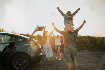 Rear view of family members enjoying with arms raised near car at picnic spot on sunny day