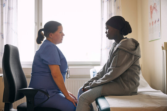Side view of female medical expert talking with teenage girl sitting on examination table in hospital