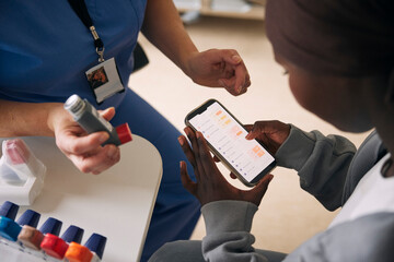 High angle view of teenage girl going through to do list app on smart phone for medical condition with female doctor in