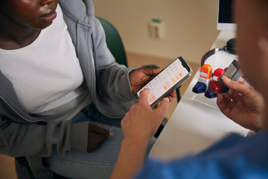 Medical expert explaining asthma inhaler features on mobile app to teenage girl in hospital