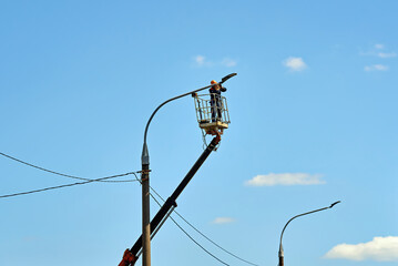 Electrician using crane platform to fix street lamp on pole, maintenance work for urban lighting...