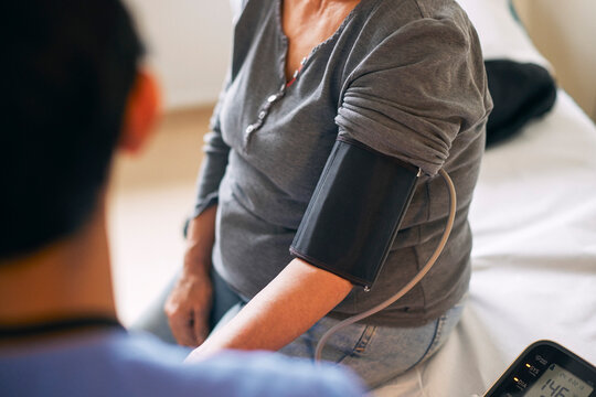 Midsection of senior woman sitting with blood pressure belt around arm during hospital visit