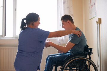 Smiling female healthcare worker stretching arm of young man with physical disability at medical clinic