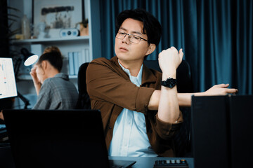 Sales manager working on desk with stretching body with arm ache at over late night time at modern...