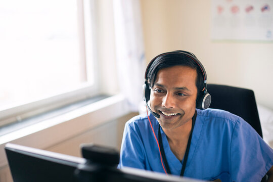 High angle view of smiling male medical expert wearing headset giving online consultation through computer in clinic