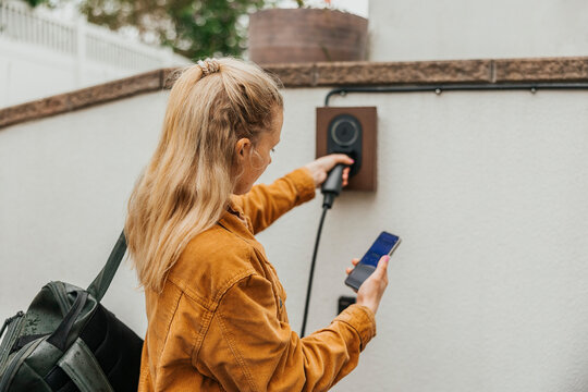 Woman with blond hair using smart phone while holding car charger