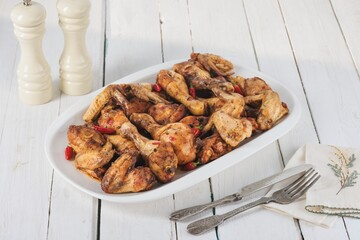Delicious and savory fried chicken parts are served hot on a platter and seasoned with chili peppers. Eating utensils are arranged at the table along with spice shakers