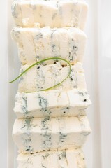 Stacked pieces of crumbly blue cheese are showcased, topped with a decorative chive. The food is...