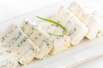 Several wedges of blue cheese are neatly arranged on a white platter, accented with a sprig of green herb. The creamy texture and striking blue veins are apparent