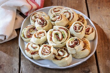 A platter overflows with golden-baked pinwheels, showcasing vibrant layers of prosciutto and pesto....