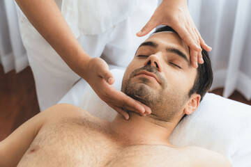 Caucasian man enjoying relaxing anti-stress head massage and pampering facial beauty skin recreation leisure in dayspa modern light ambient at luxury resort or hotel spa salon. Quiescent