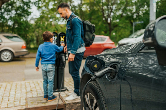 Power cable charging electric car with father and son standing in background