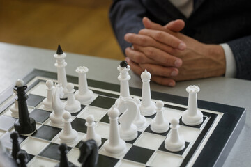 Grandmaster with folded hands studies a crowded chessboard; white army readies the next...