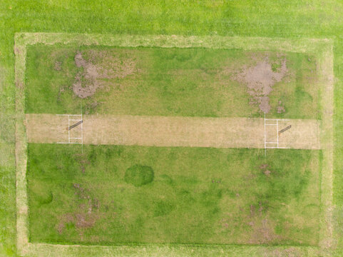 Aerial view showing dirt cricket pitch with white crease lines and wickets at cricket ground