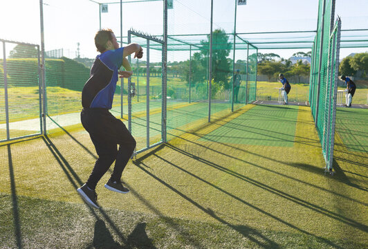 Diverse male teammates practicing bowling and batting with cricket ball in cricket nets