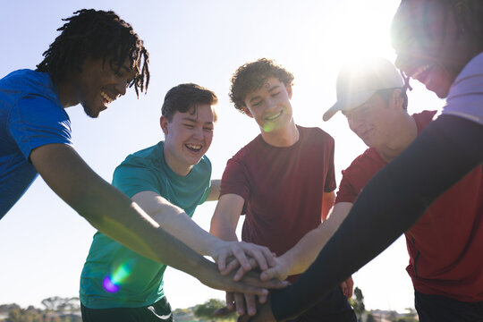 Diverse male teammates placing stacked hands and forming pre-game huddle on grassy field