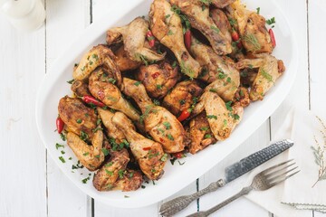 Roasted chicken pieces, including wings and drumsticks, are presented on a white platter. Red peppers and fresh herbs add a vibrant touch to this savory dish, ready to be served