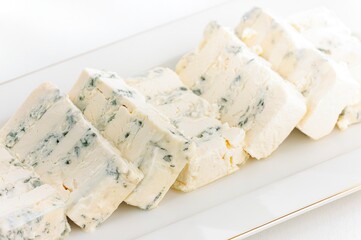 Wedges of creamy white gorgonzola cheese, speckled with blue veins, sit elegantly on a gleaming white platter. The delicate setting evokes a sense of refined indulgence