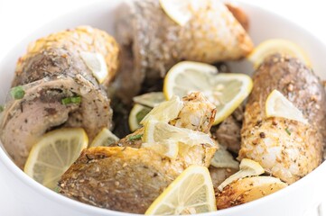 Chicken pieces are baked with lemon slices and herbs and spices, nestled inside a white bowl. The...
