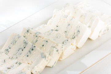 Delicate slices of rich Stilton cheese are arranged on a pristine white platter. The blue veining whispers of bold flavors, inviting a tasting adventure for cheese connoisseurs