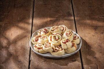 Freshly baked pinwheels are resting on a speckled plate atop a rustic wooden table. The appetizing...