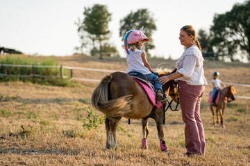 mom and little baby girl playing while horseback riding outdoors in ranch. children and horse riding