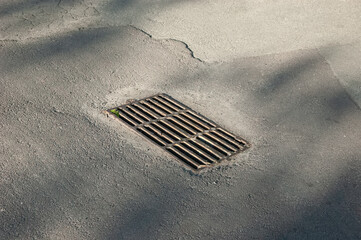 A storm drain grate set in old asphalt with cracks and worn textures around it.