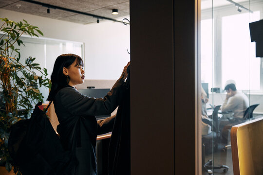 Female entrepreneur hanging jacket on coat hook while entering in office