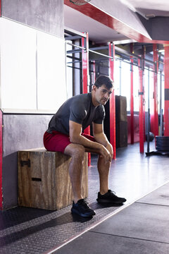 Man resting on wooden plyometric box at gym next to rig and weight plates on rubber mats